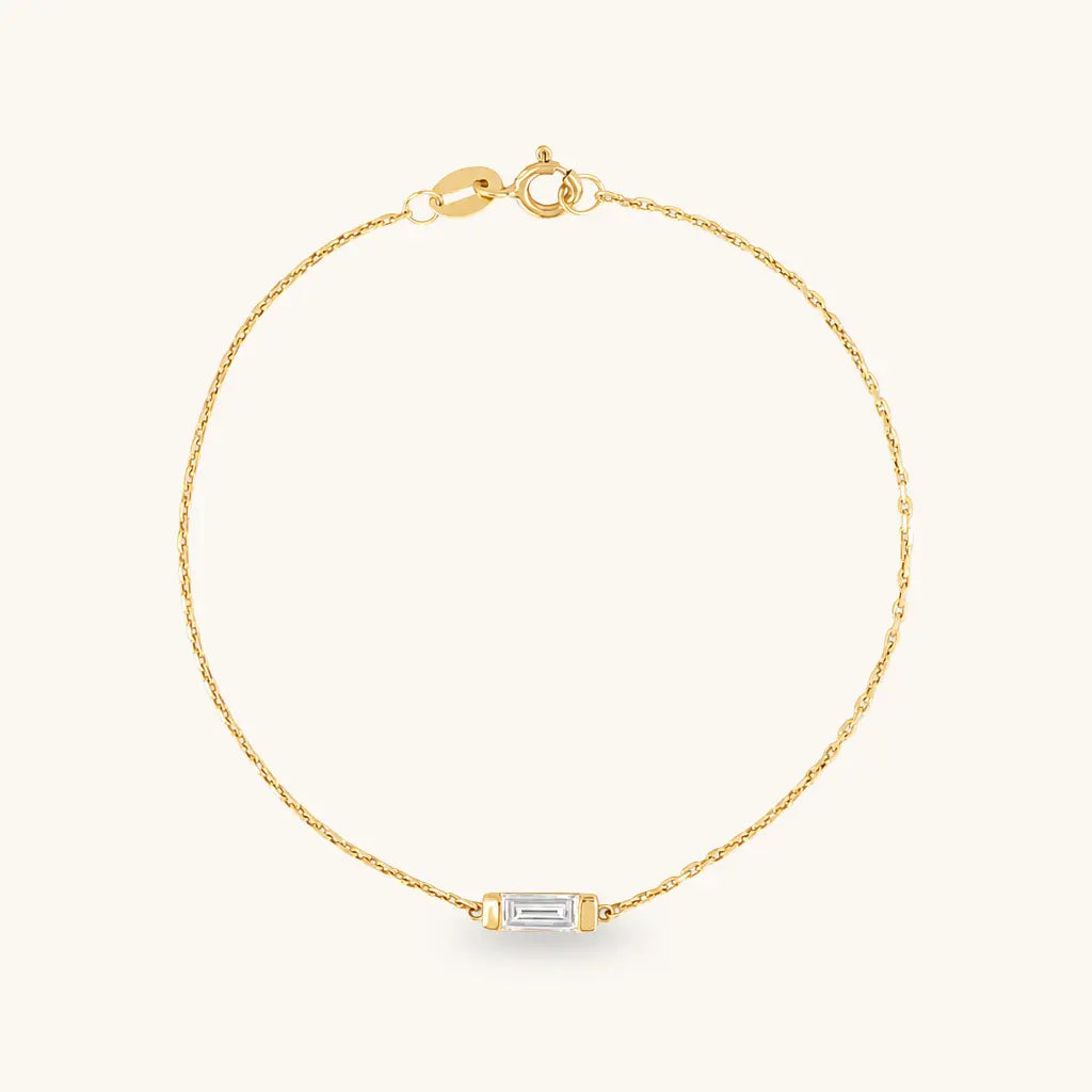 A delicate yellow gold chain bracelet with a small rectangular baguette-cut clear gemstone set in gold at the center, displayed on a clean off-white background.