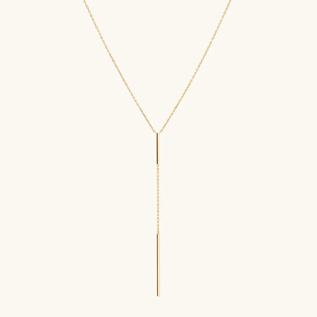 A delicate gold Y-necklace with a fine chain and a slim vertical bar pendant, displayed against a solid off-white background.
