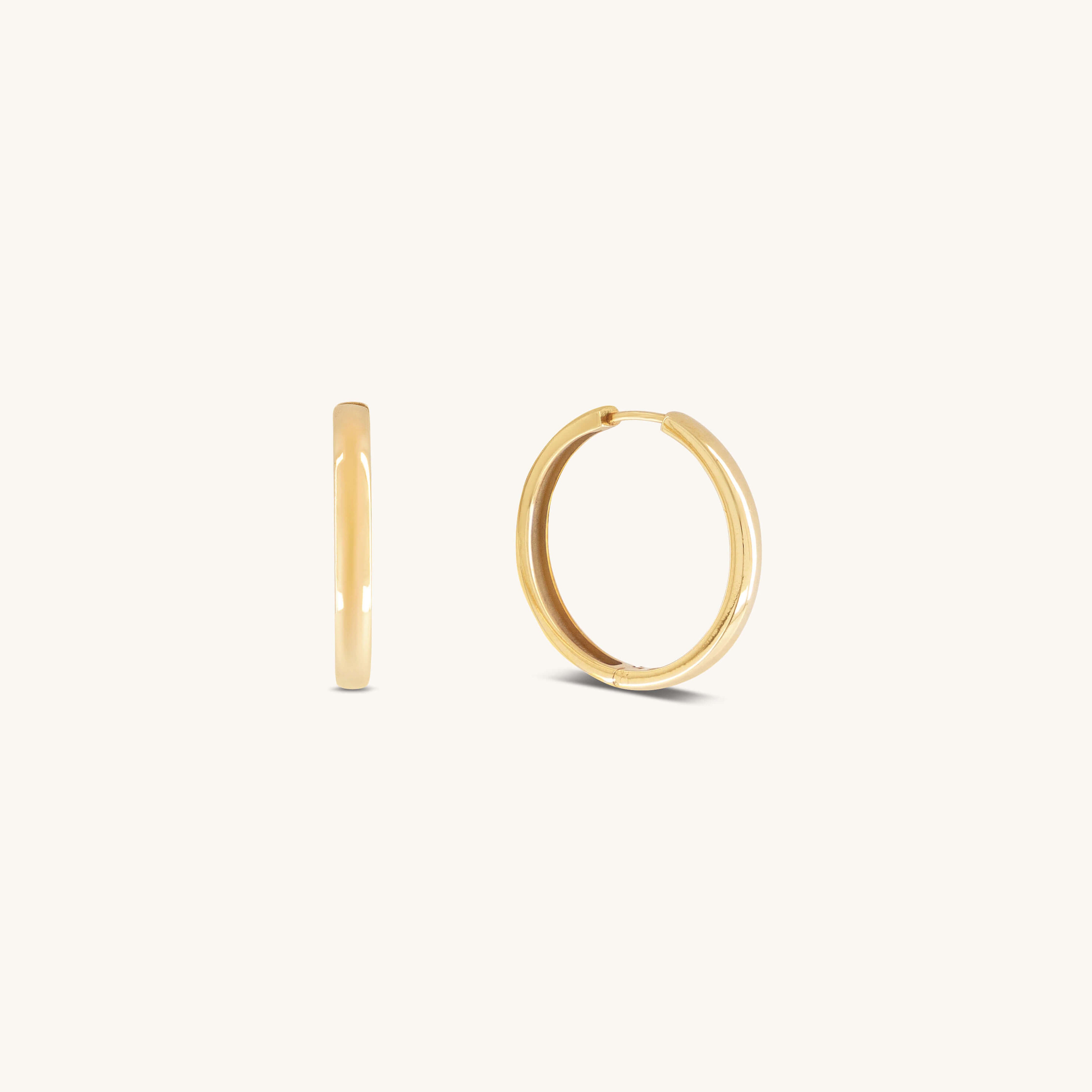 Two small, simple Gertrude Hoops by Glasâje are shown on a plain, light background—crafted in 9ct solid gold with a 23mm diameter. One earring is displayed from the side and the other from the front.