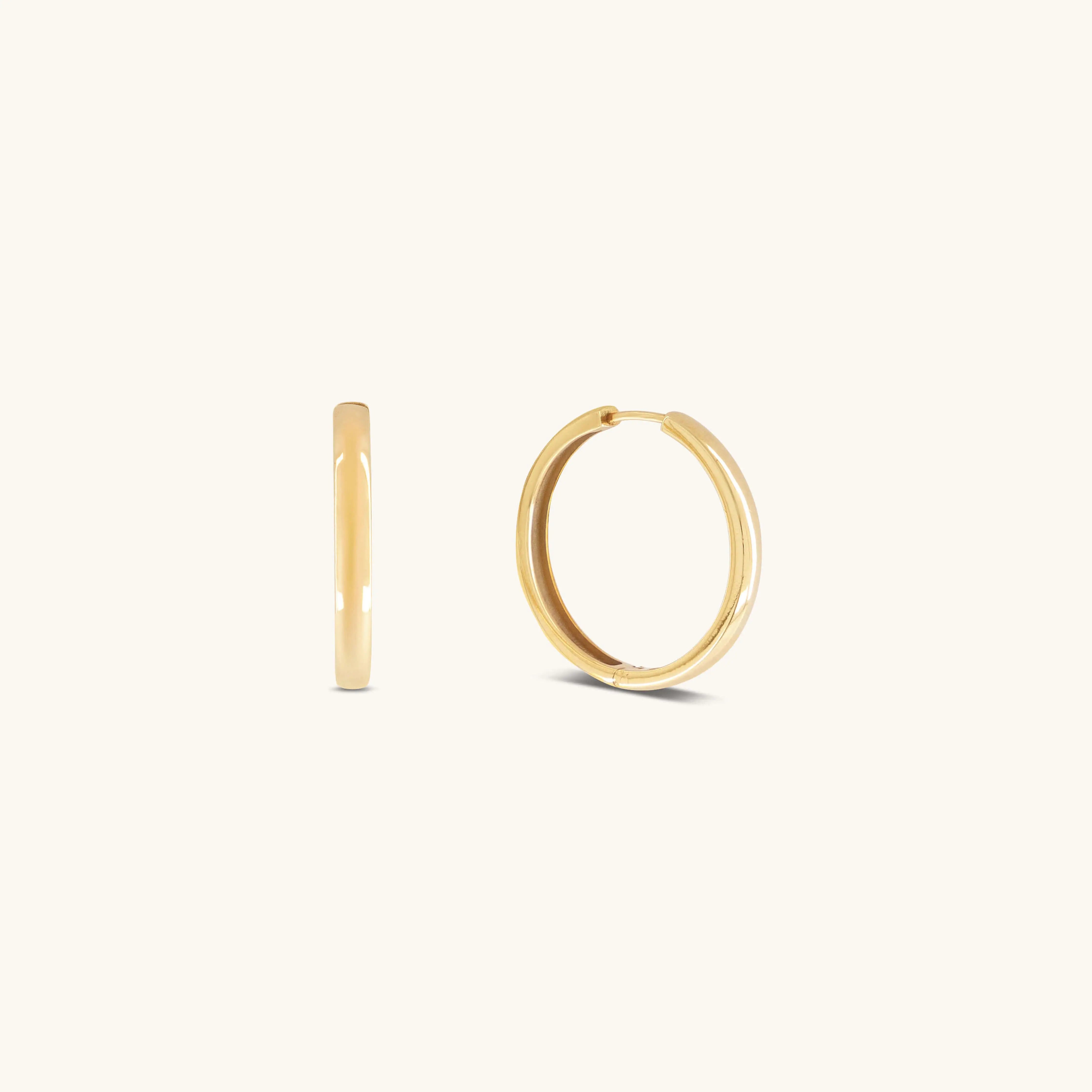 Two small, simple Gertrude Hoops by Glasâje are shown on a plain, light background—crafted in 9ct solid gold with a 23mm diameter. One earring is displayed from the side and the other from the front.