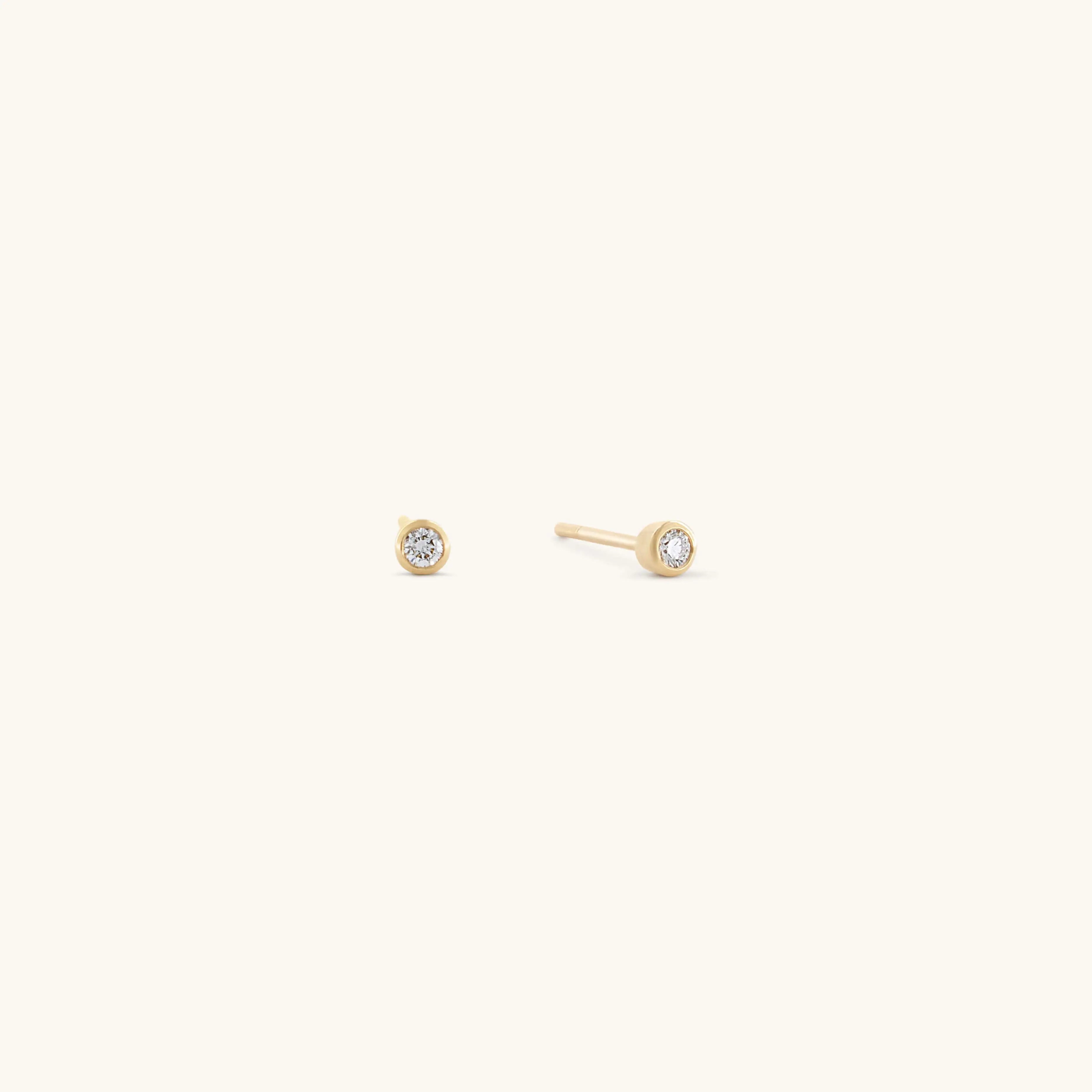 The Glasâje Satellite Studs feature small, round solid gold settings with a central clear gemstone, elegantly showcased against a plain light background.
