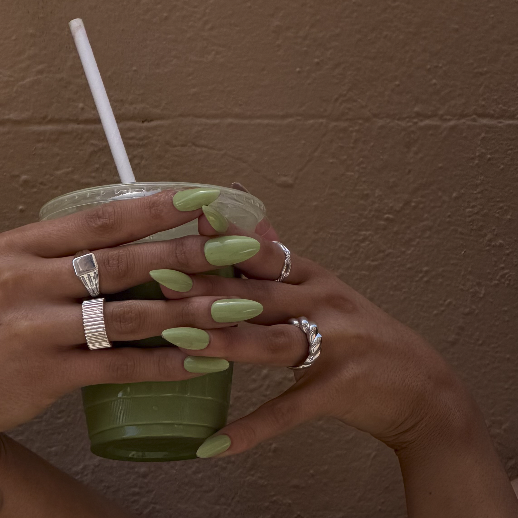 Hands with green nail polish holding a green cup against a brown wall