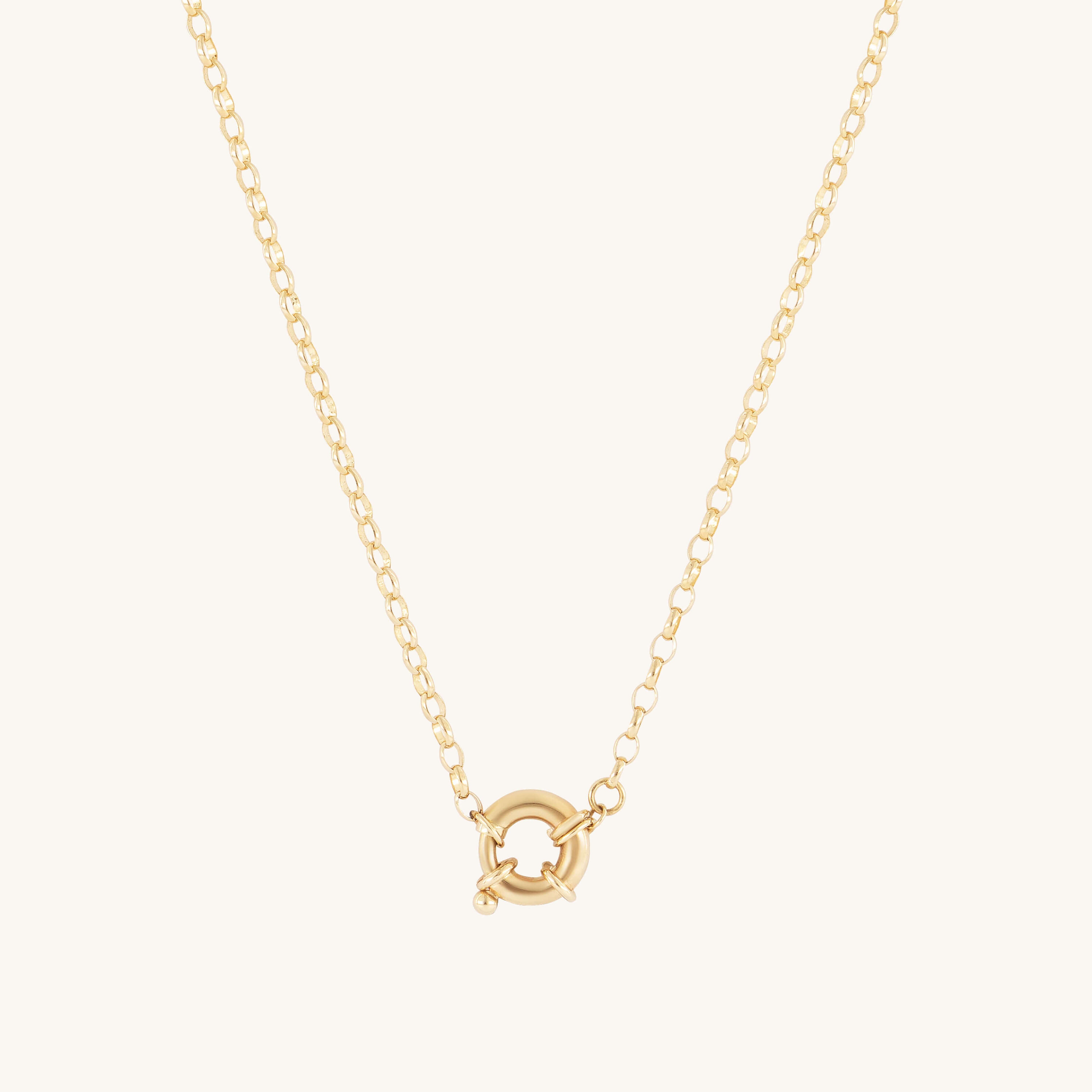 The Glasâje Hosier Necklace features a gold belcher chain with a small circular spring ring clasp pendant at the center, set against an off-white background.