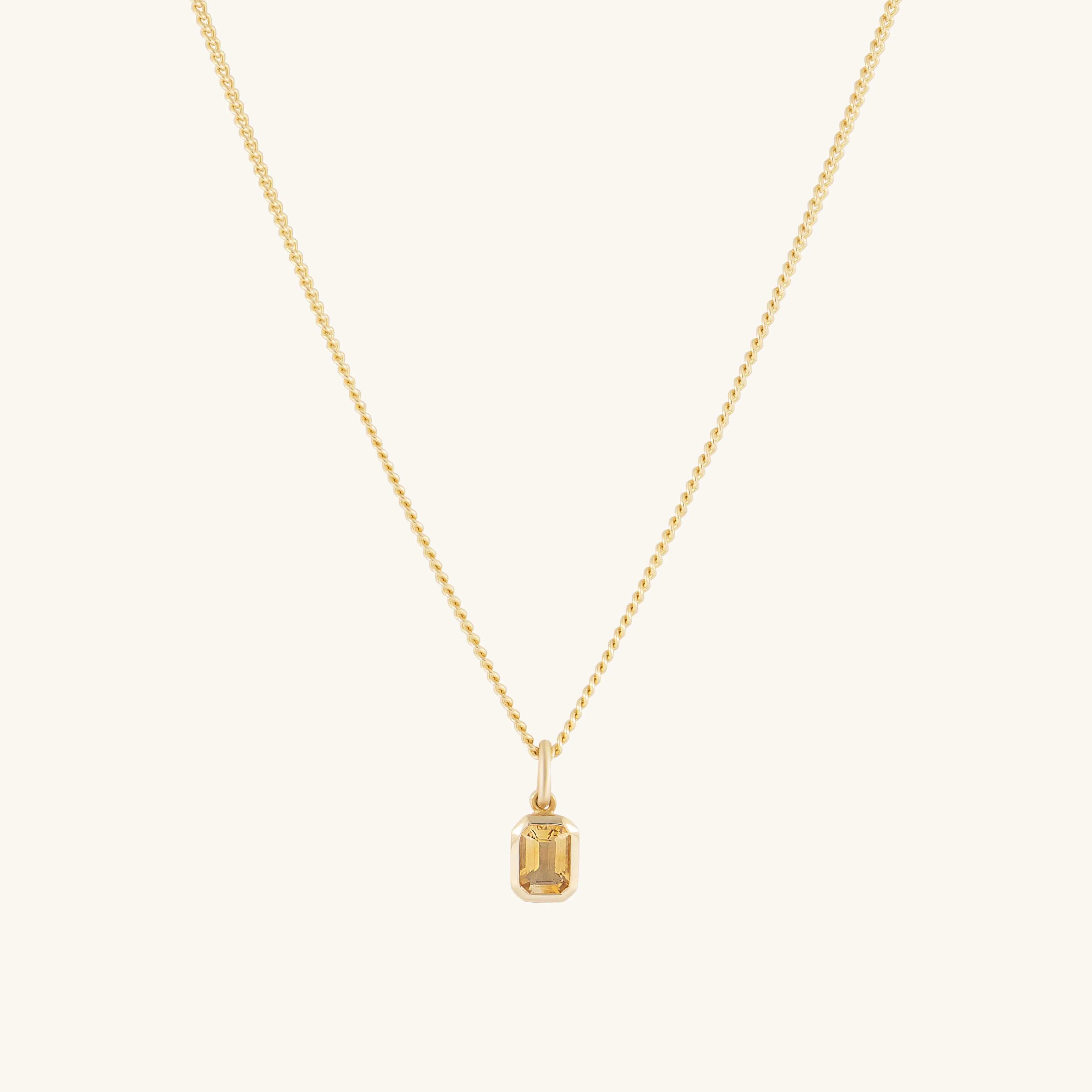 A fine gold chain necklace featuring a small rectangular pendant with an emerald-cut auburn citrine. Understated and elegant, the pendant stands out subtly against a simple backdrop.