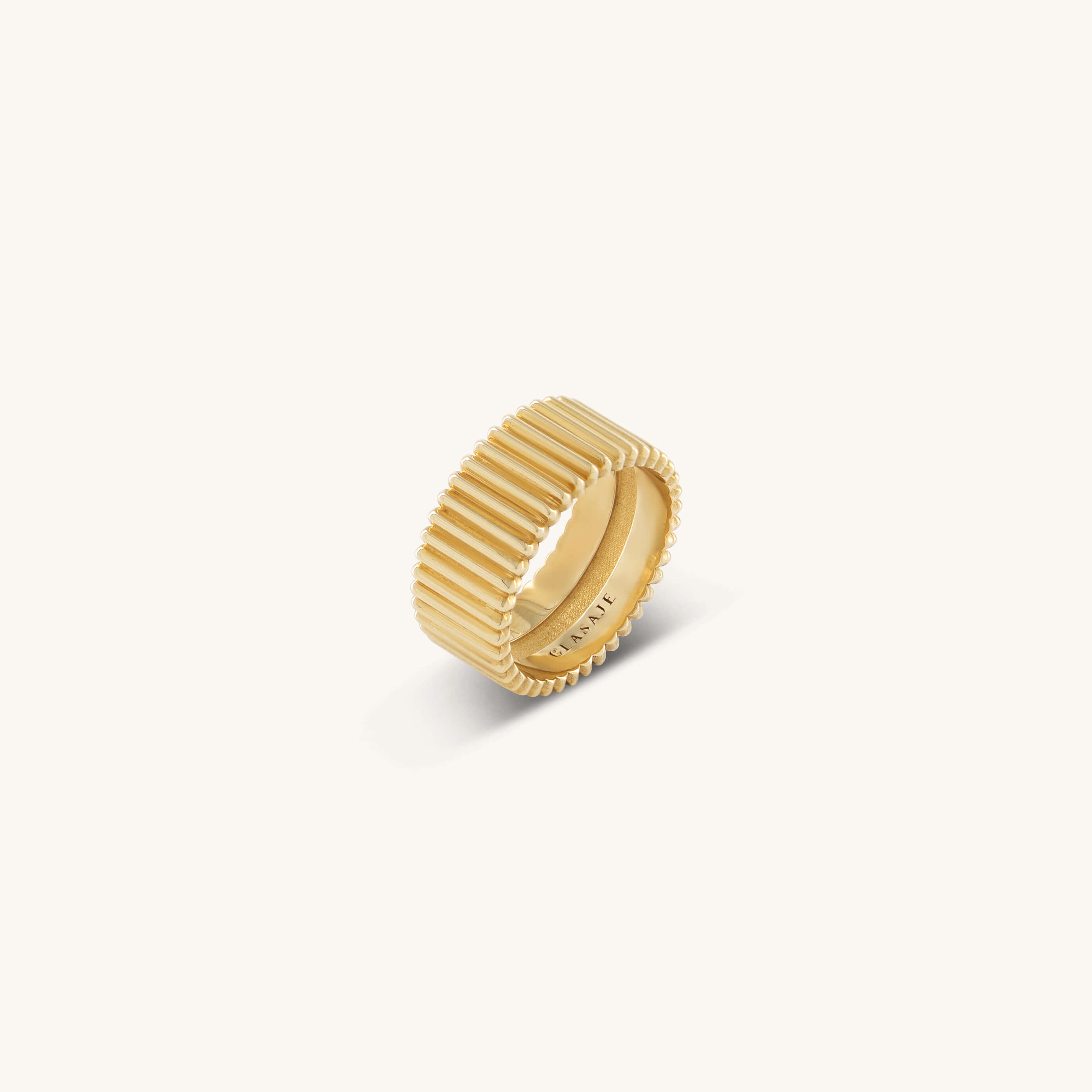 A textured gold ring with vertical grooves and a smooth inner band is centered against a plain white background, conveying elegance and simplicity.