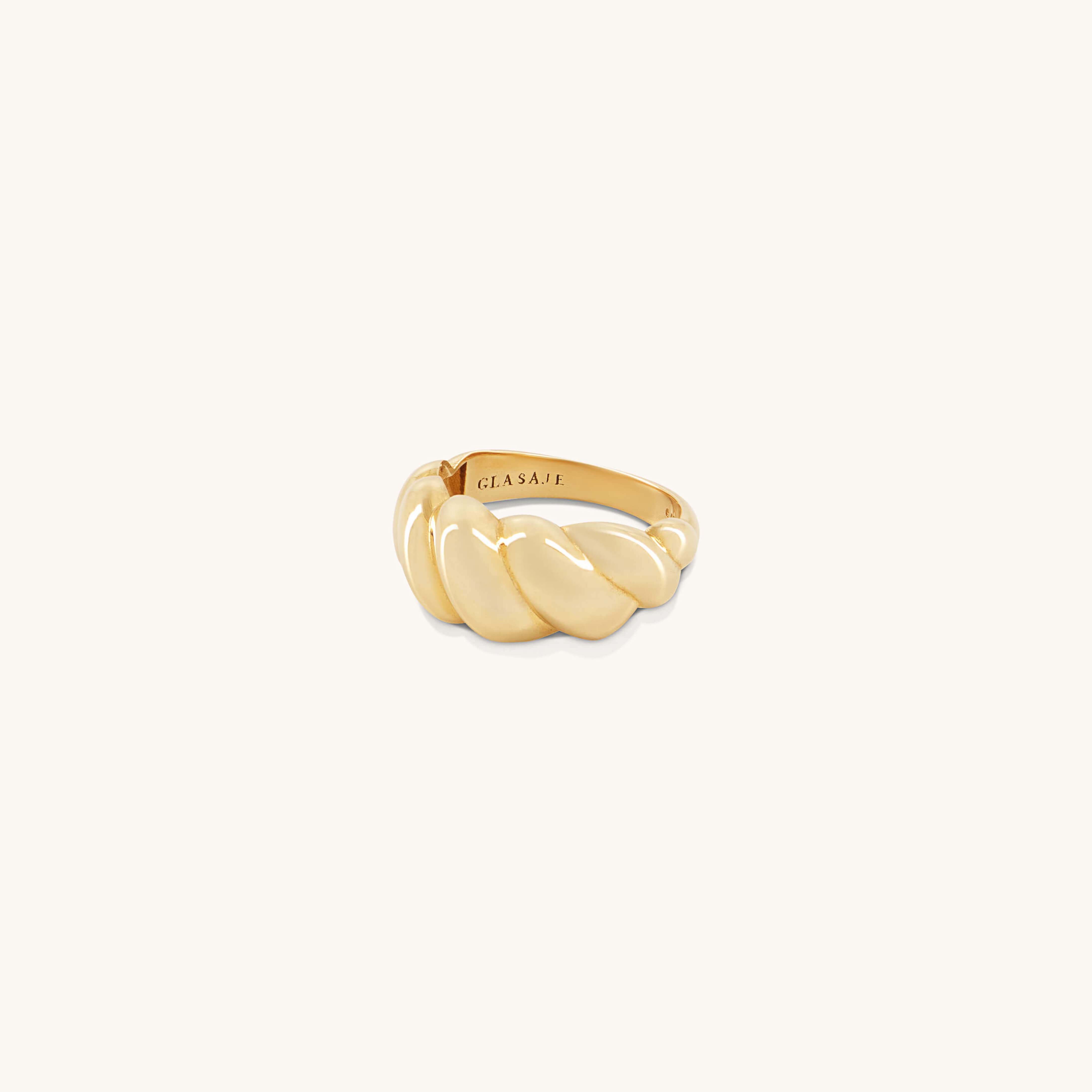 A gold, twisted croissant-shaped Lune Ring with a polished finish is displayed on a plain background. The inner band features the brand name Glasâje engraved.