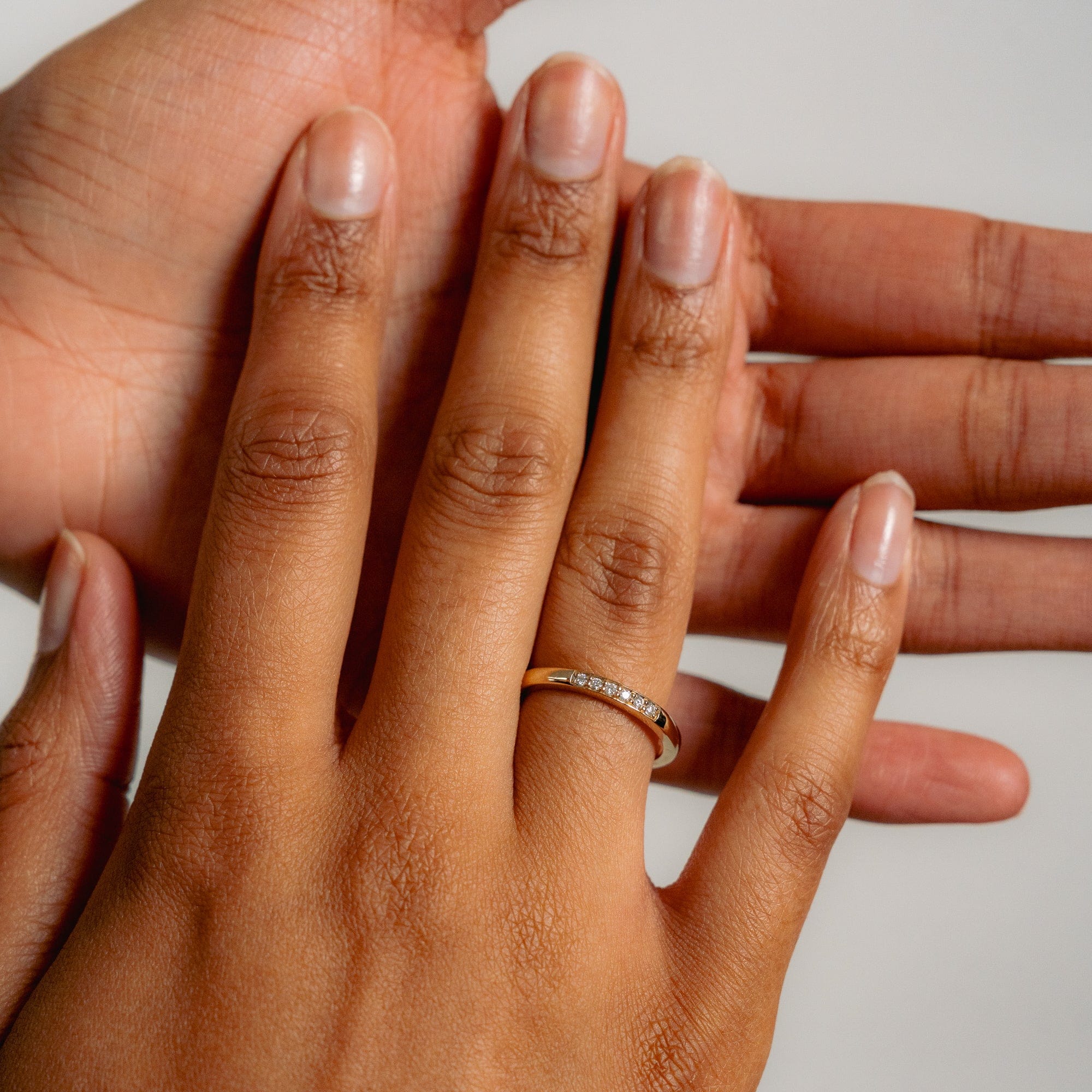 Close-up of a hand wearing a gold ring with six diamonds, gently held by another hand. The image conveys warmth and affection.