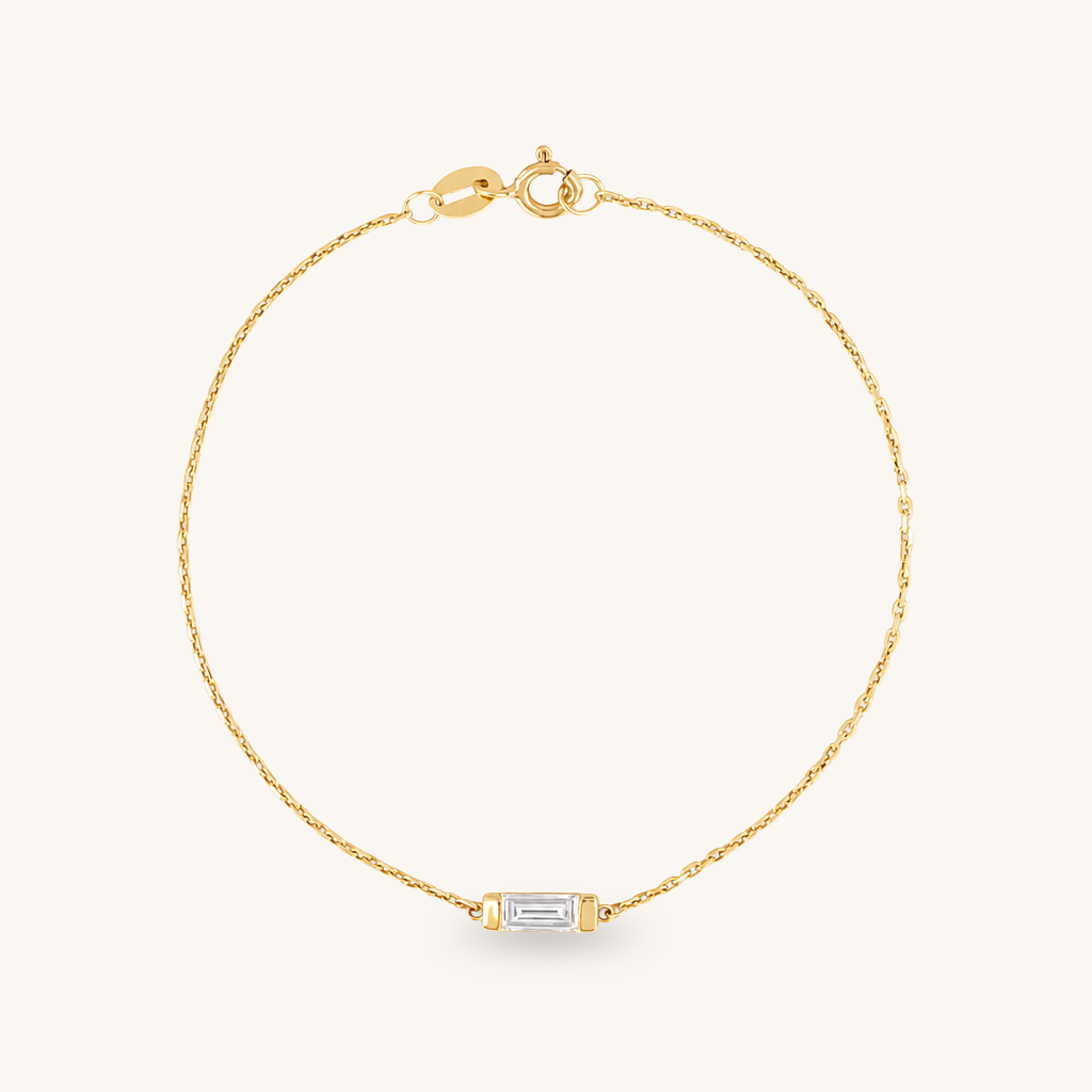 A delicate yellow gold chain bracelet with a small rectangular baguette-cut clear gemstone set in gold at the center, displayed on a clean off-white background.