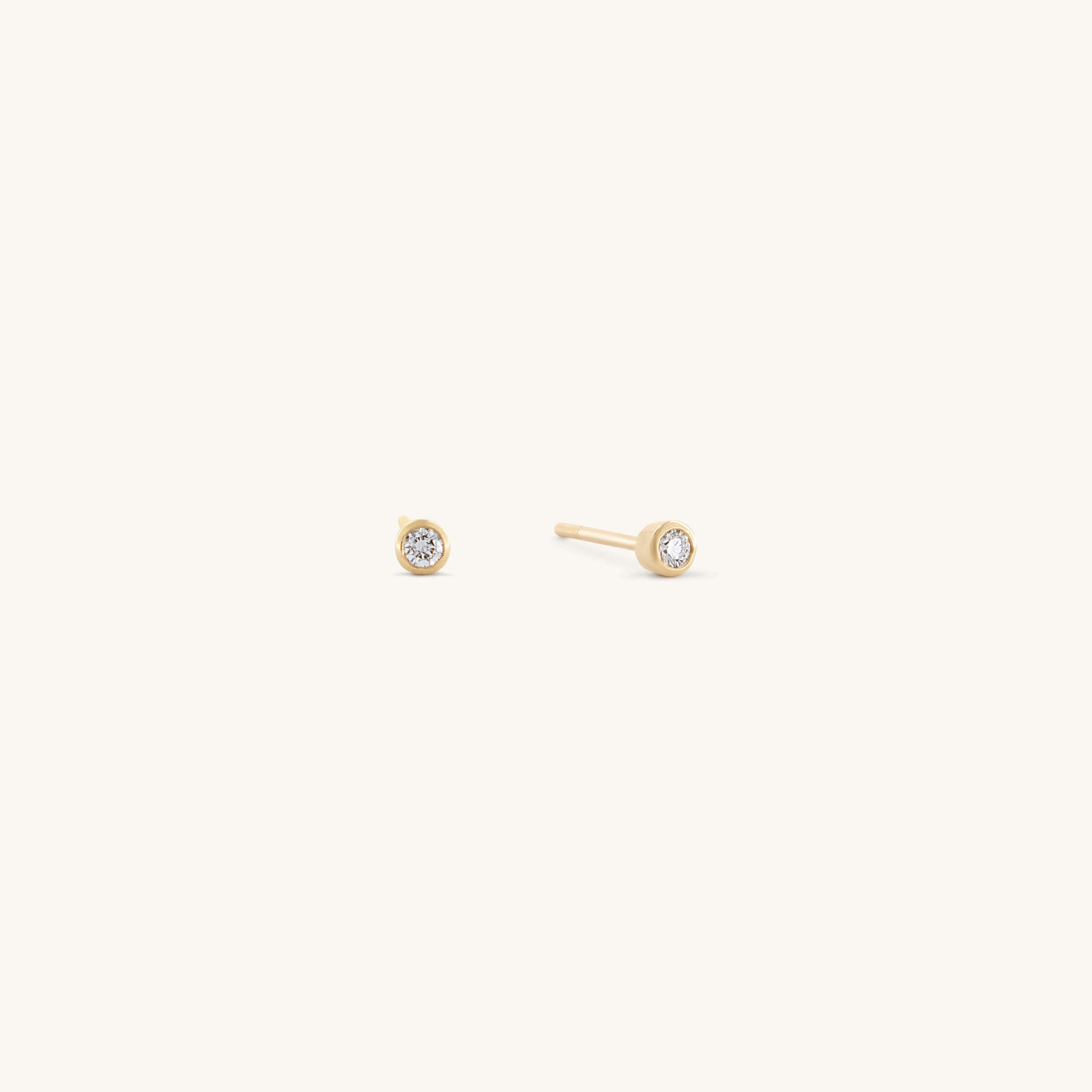 The Glasâje Satellite Studs feature small, round solid gold settings with a central clear gemstone, elegantly showcased against a plain light background.
