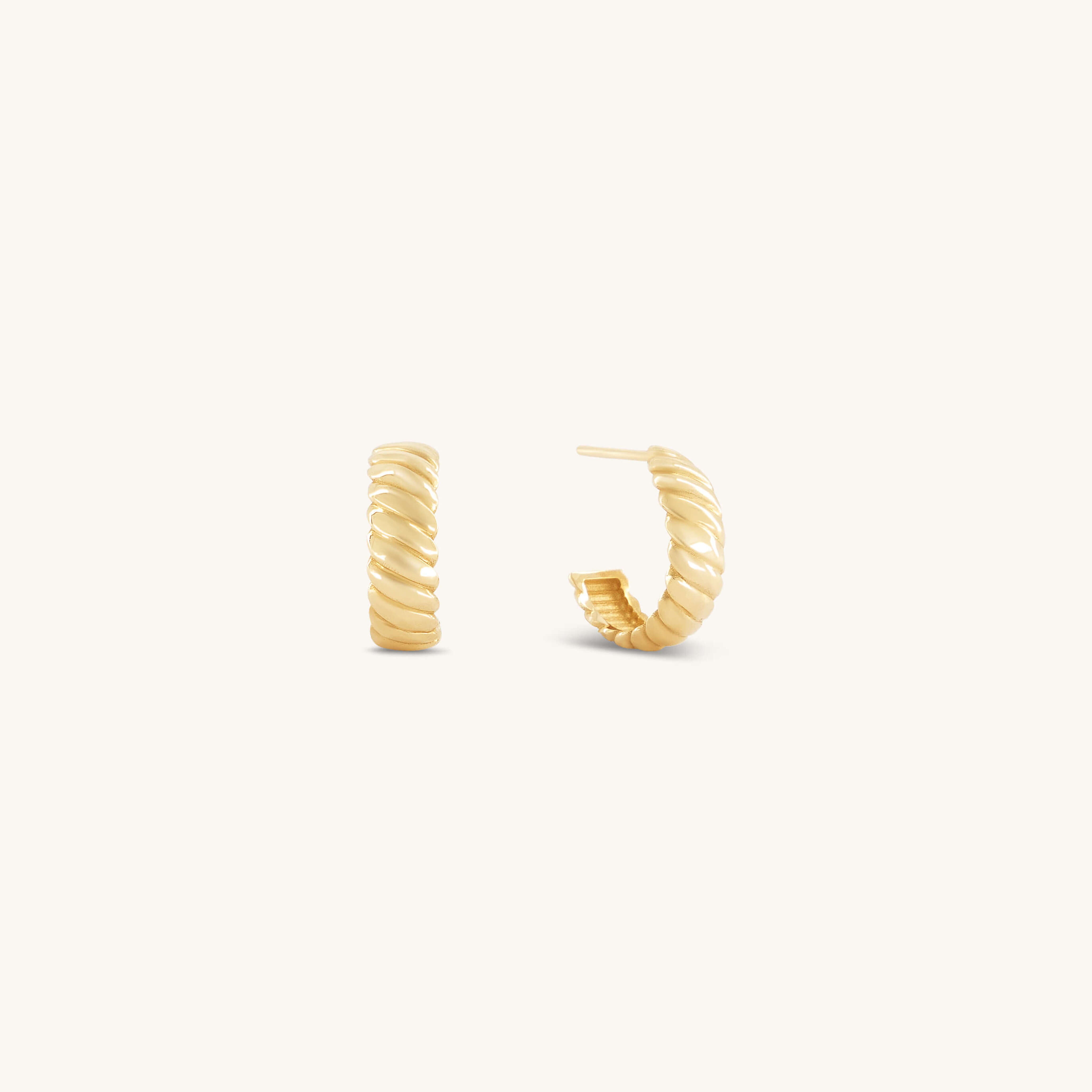 Gold hoop earrings with a twisted design are set against a white background. They convey a sense of elegance and simplicity, highlighting their textured surface.