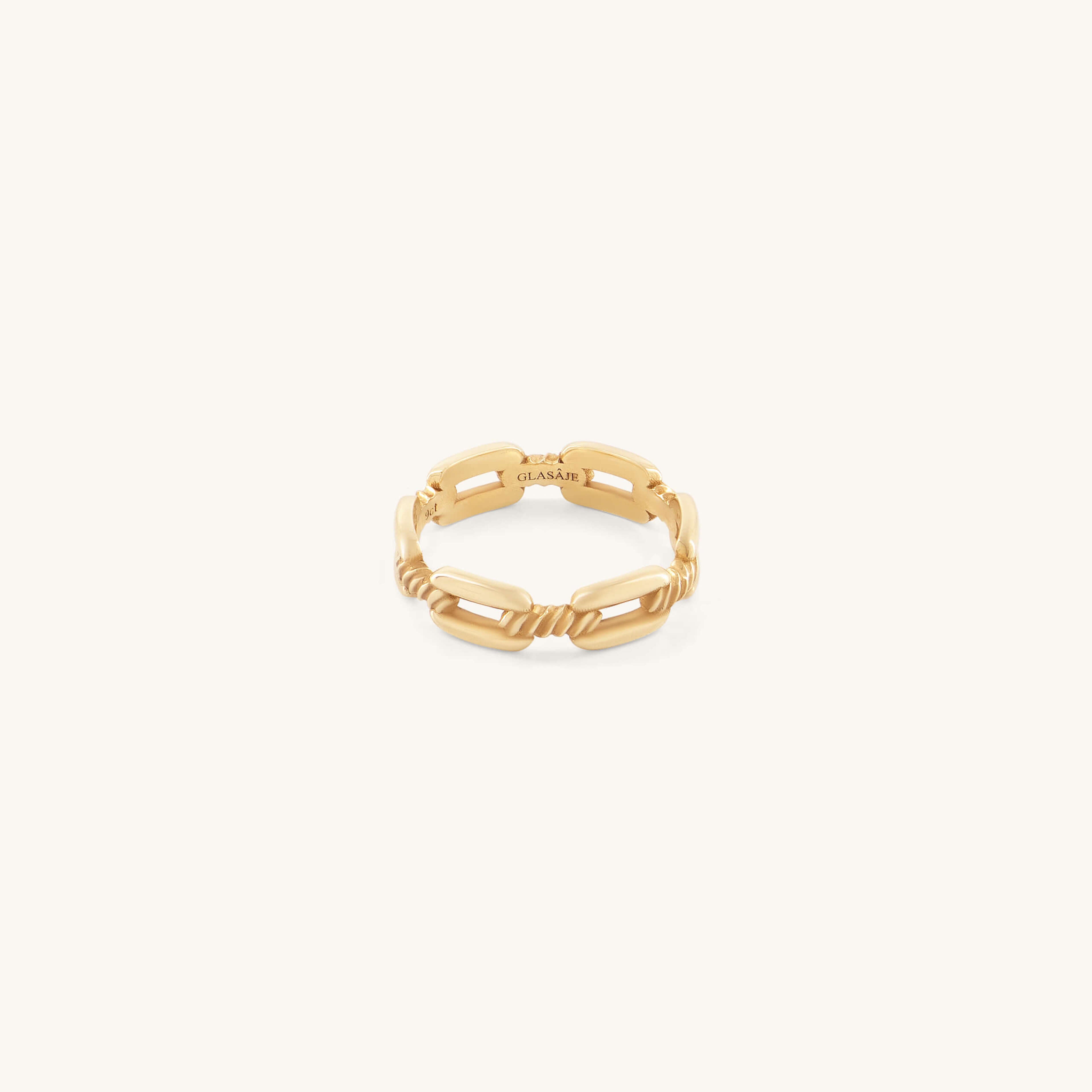 A delicate gold ring with a chain-link design on a soft cream background. The ring's intertwined pattern conveys elegance and modern style.