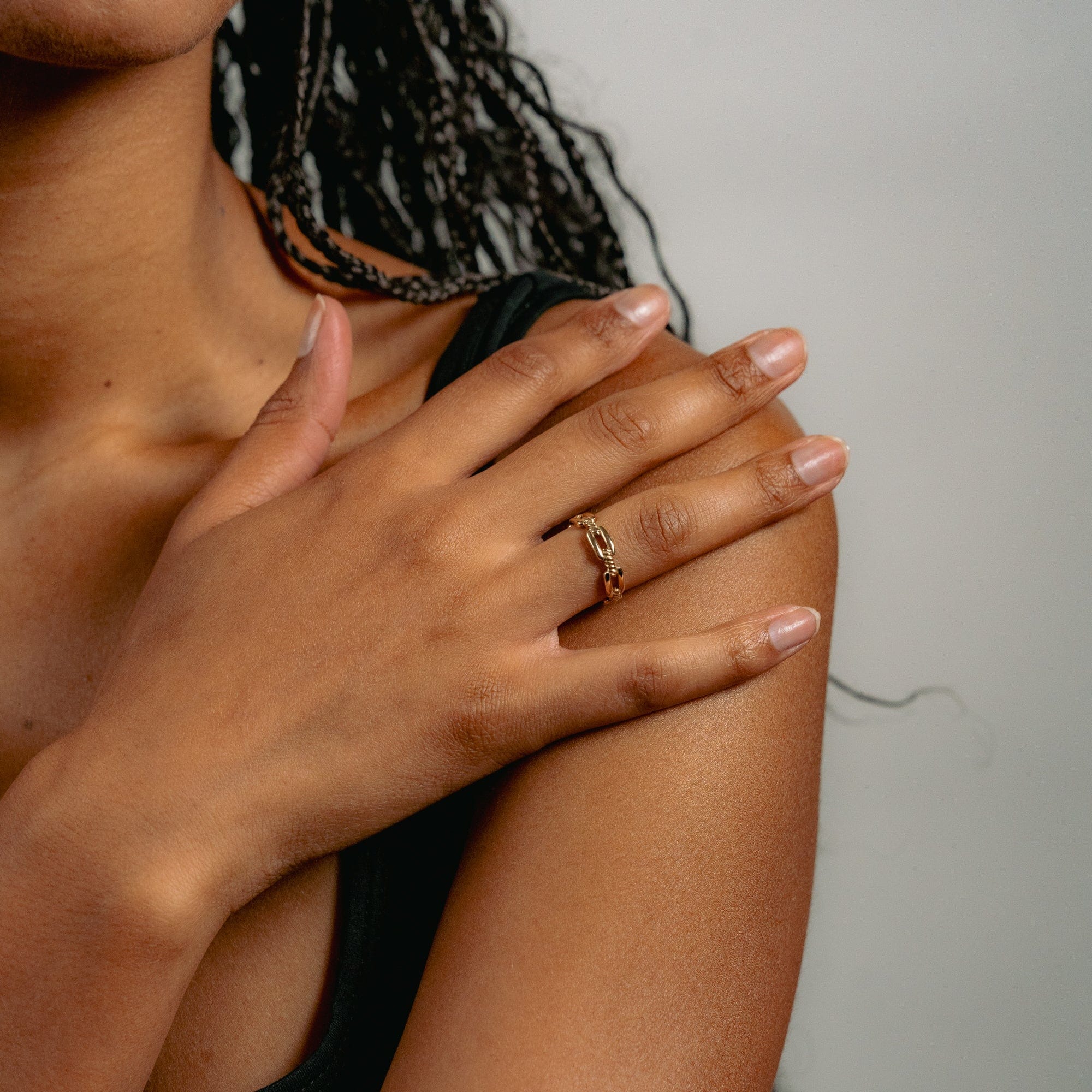 Close-up of a person with braided hair, wearing a gold ring on their finger. They touch their shoulder gently, conveying a calm and serene atmosphere.