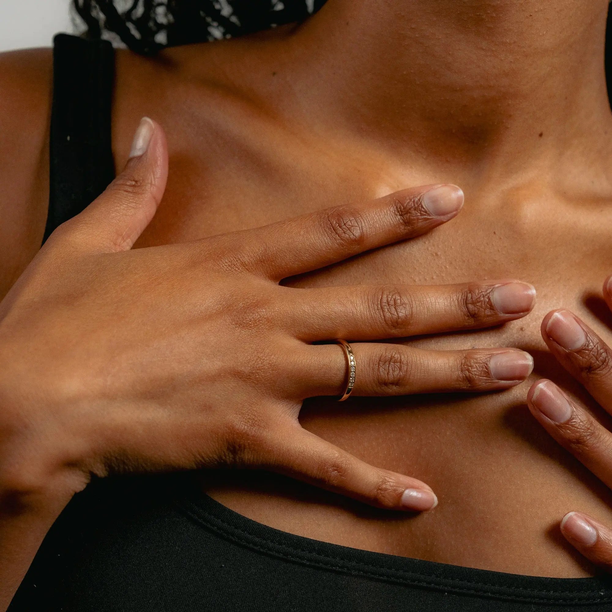 Close-up of a person wearing a black top, with hands touching their chest. A gold ring adorns one finger. The image conveys a sense of calm.