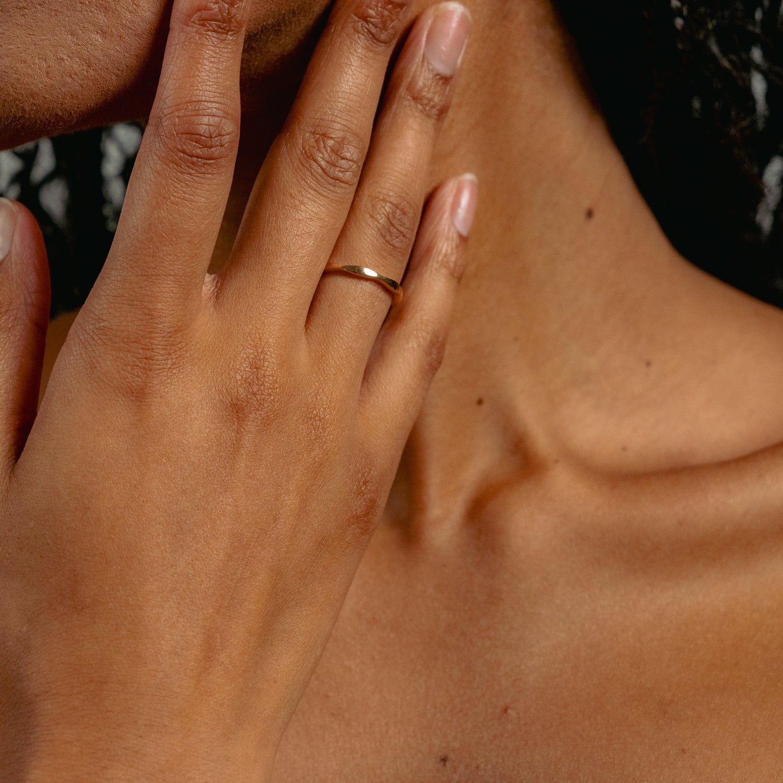 A close-up of a hand gently touching the face, highlighting smooth skin and natural nails, showcases Glasâje’s Ripple Stacking Ring—a 9ct solid gold band with a minimal ripple design—alongside the collarbone and neck.